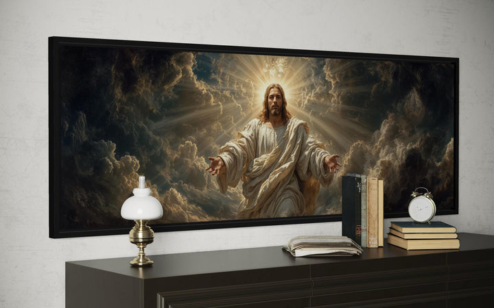Panoramic canvas print of Jesus with open arms and radiant light, framed on a dark console table.