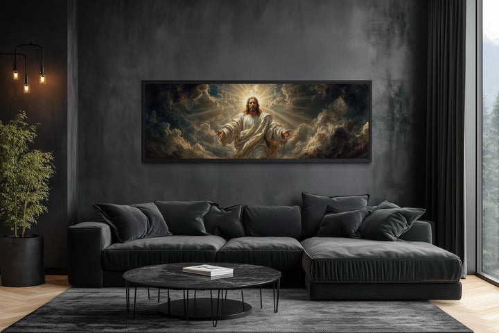 Panoramic canvas print of Jesus with open arms centered on a dark wall above a modern black sofa.