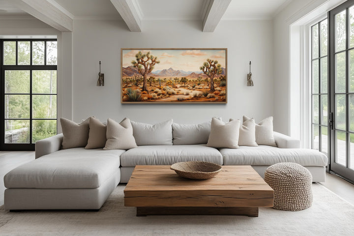 Framed Joshua tree desert landscape canvas painting hanging above a neutral sectional sofa.