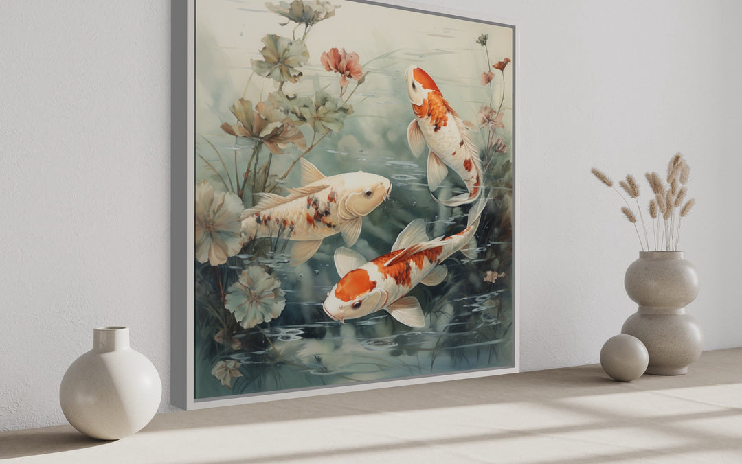 Square framed canvas art of orange and white koi fish swimming in a sage green pond with lilies.