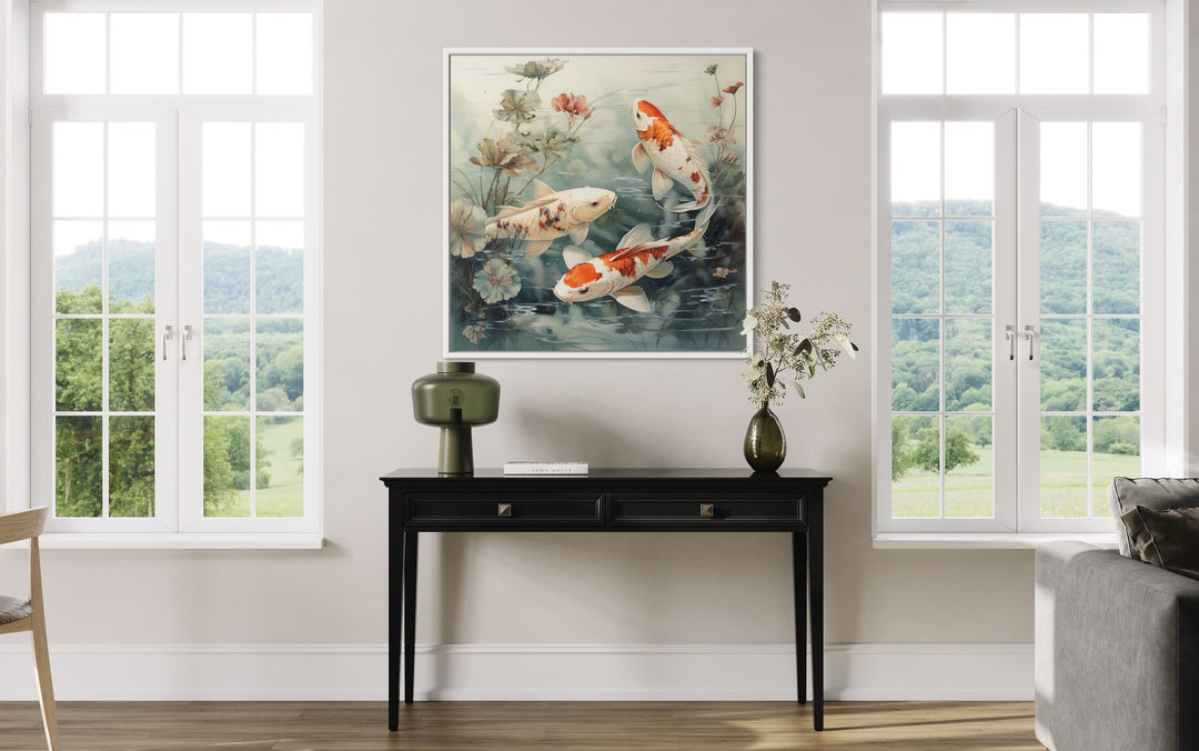 Square framed canvas wall art of koi fish swimming in a sage green pond above a black console table.