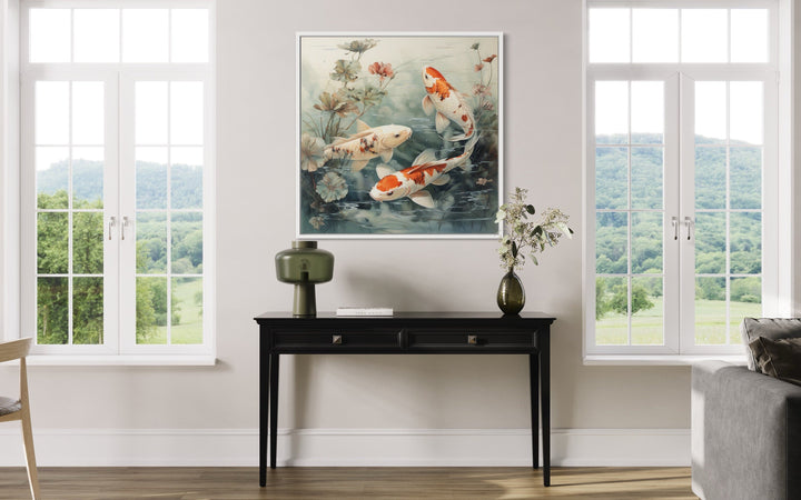 Square framed canvas wall art of koi fish swimming in a sage green pond above a black console table.