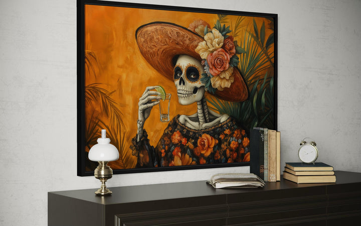 Mexican canvas wall art of La Calavera Catrina drinking tequila in a black frame.