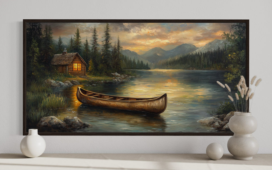 Panoramic canvas art of a rustic canoe on a lake with a cabin and mountains at sunset.