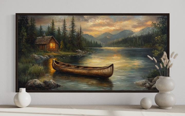 Panoramic canvas art of a rustic canoe on a lake with a cabin and mountains at sunset.