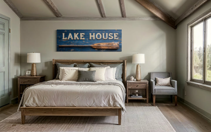 Rustic blue Lake House sign with a wooden oar on a horizontal framed canvas above a bed.