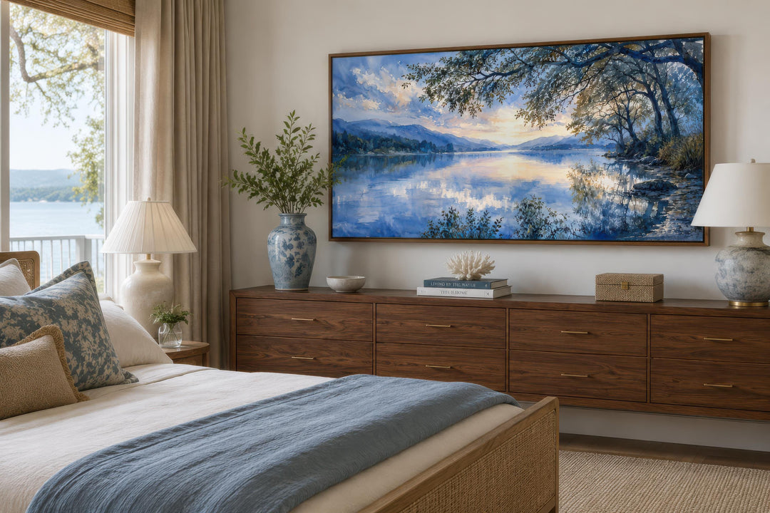 Framed horizontal canvas print of a blue lake landscape hanging above a wooden dresser in a bedroom.