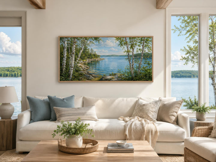 Wide horizontal birch tree canvas print of a calm lake scene hanging above a white sofa.