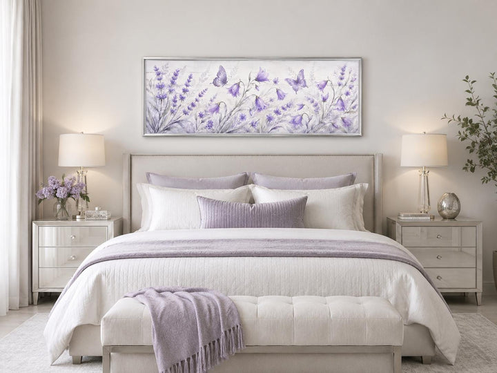 Long horizontal canvas art of lavender wildflowers and butterflies above a bed in a neutral room.
