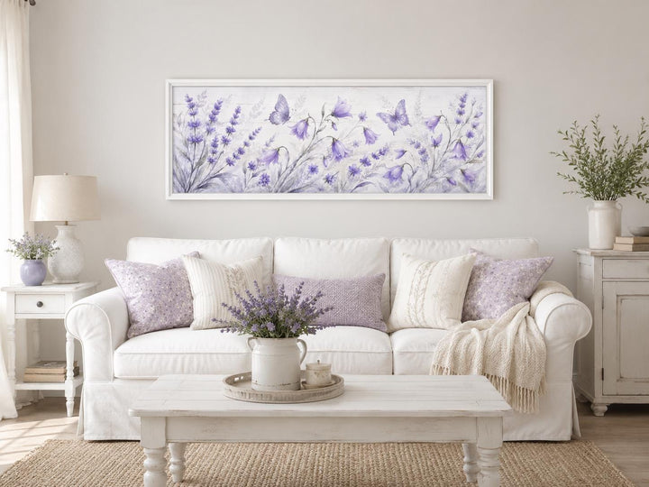 Long horizontal canvas art of lavender wildflowers and butterflies above a white sofa.
