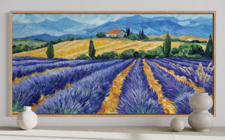A panoramic canvas print of a lavender field painting in a light wood frame on a neutral wall.
