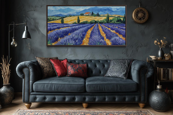 A panoramic canvas print of a lavender field hangs above a dark tufted sofa in a rustic room.