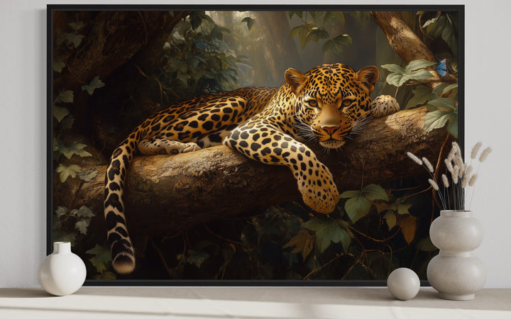 Framed canvas wall art of a leopard resting on a tree branch in a lush jungle setting.
