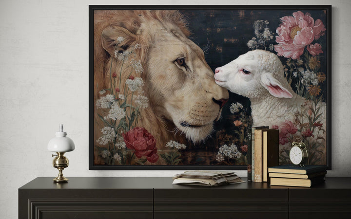Lion and lamb framed canvas wall art with floral accents on a dark sideboard with books and a lamp.