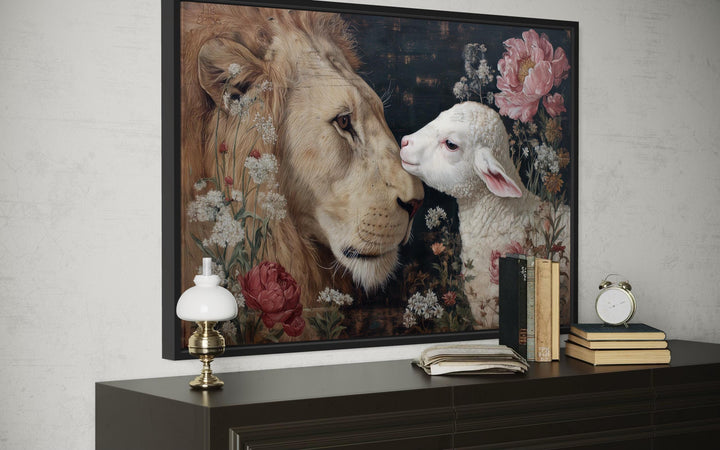 Lion and lamb framed canvas wall art with floral accents on a dark dresser with books and a lamp.
