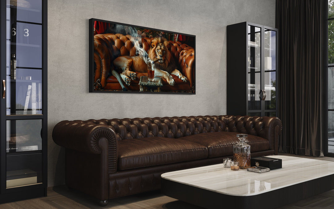 Lion On The Couch Smoking Cigar Framed Canvas Print hanging above a brown leather chesterfield sofa.