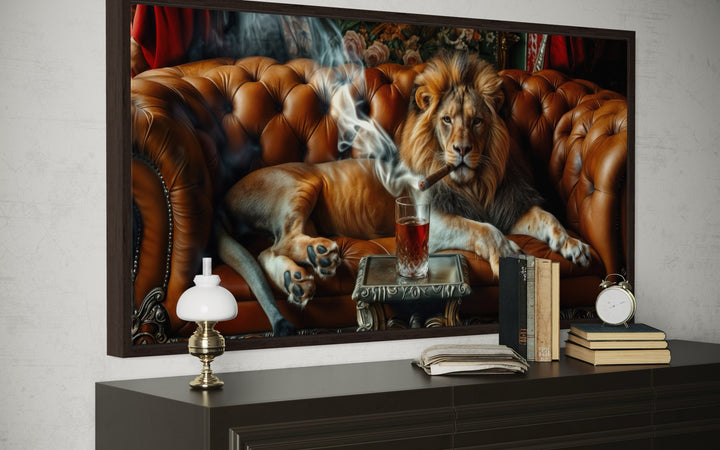 Framed canvas print of a lion smoking a cigar on a leather couch, displayed above a dark sideboard.
