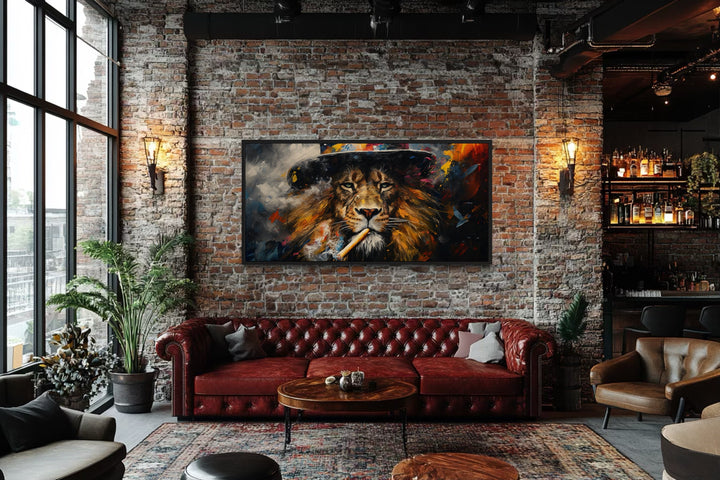Framed canvas print of a lion smoking a cigar on a brick wall above a red leather sofa.