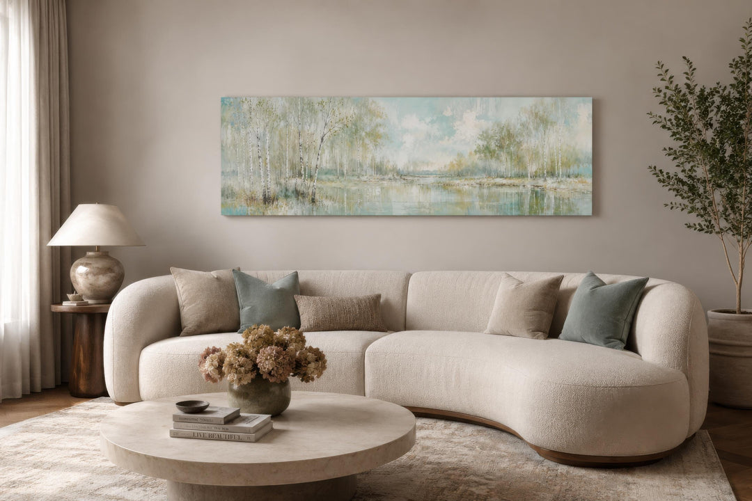 Long horizontal canvas print of birch trees in soft sage green above a modern curved sofa.