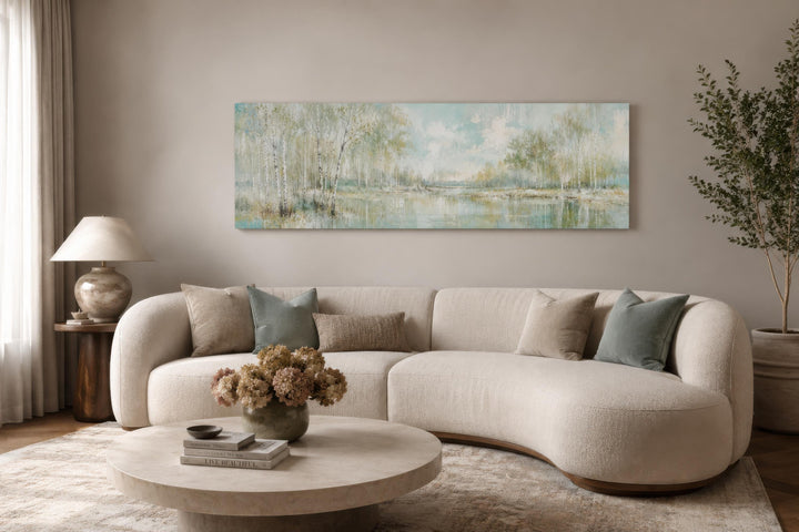 Long horizontal canvas print of birch trees in soft sage green above a modern curved sofa.