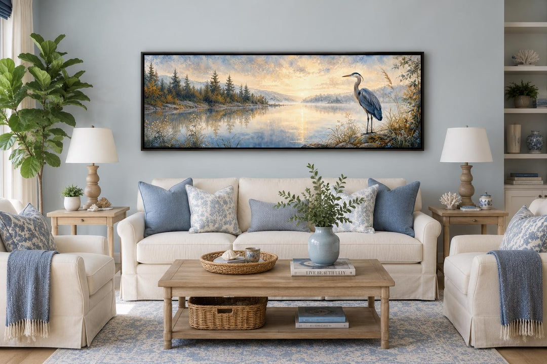 Long horizontal canvas wall art of a blue heron by a misty lake at dawn above a living room sofa.