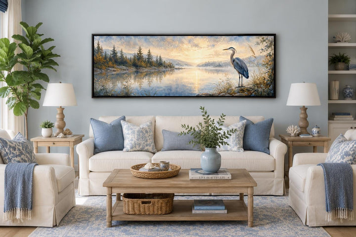 Long horizontal canvas wall art of a blue heron by a misty lake at dawn above a living room sofa.