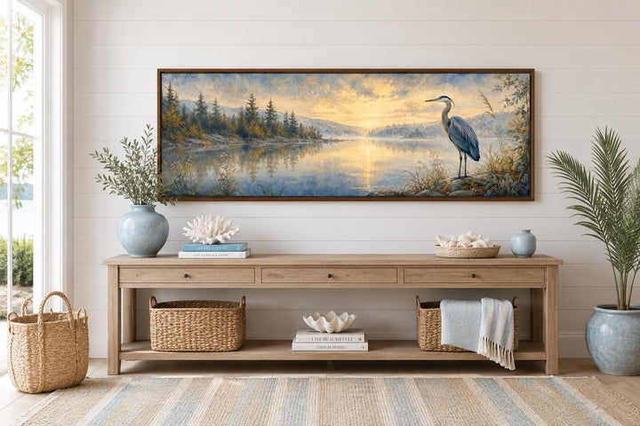 Long horizontal canvas wall art of a blue heron by a misty lake at dawn above a wooden console.