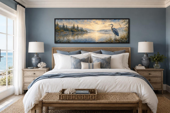 Long horizontal canvas art of a blue heron by a misty lake at dawn, hung above a bed.