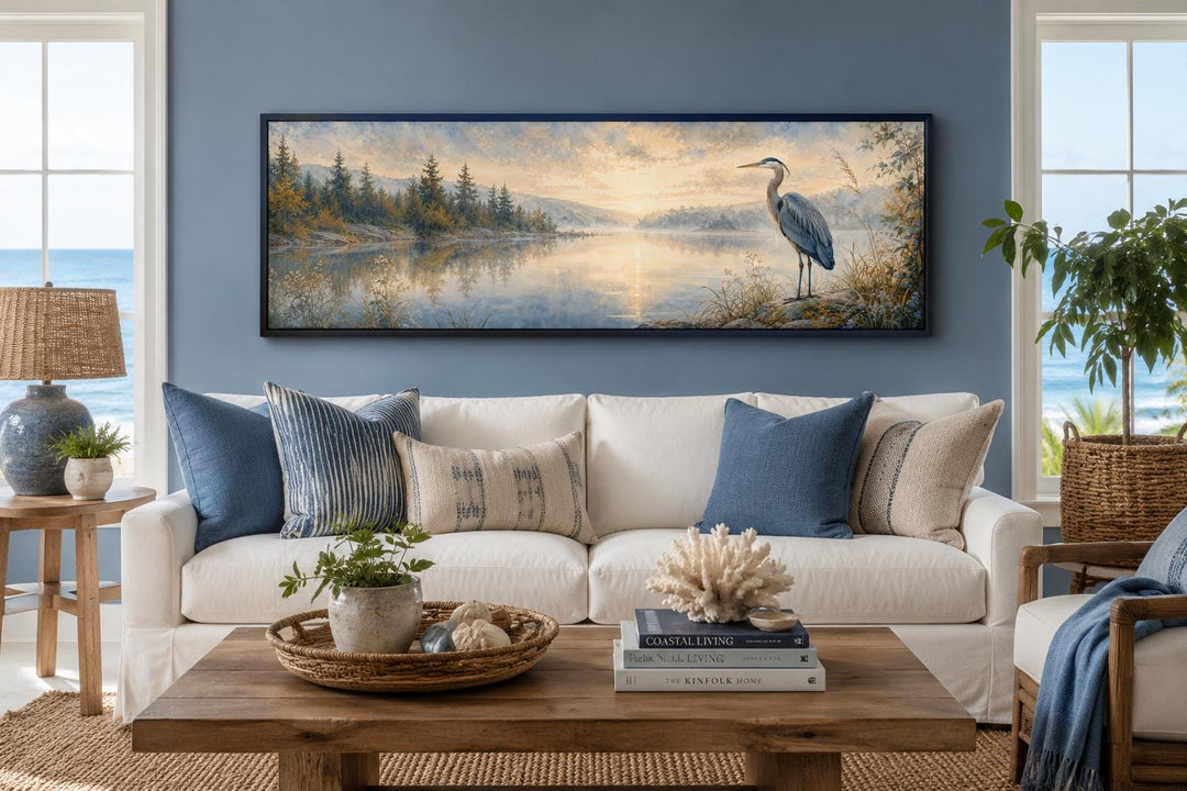 Long horizontal canvas art of a blue heron by a misty lake at dawn, hung above a white sofa.