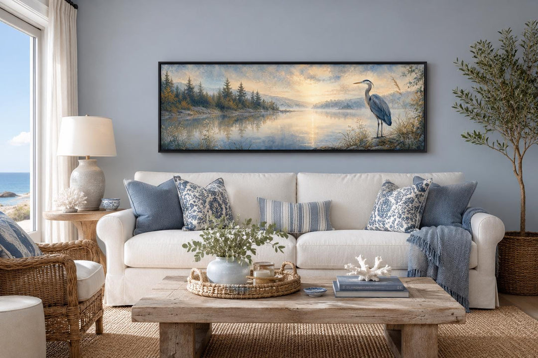 Long horizontal canvas wall art of a blue heron by a misty lake at dawn above a white sofa.