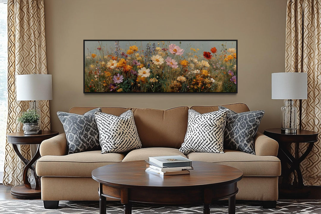 Long horizontal painting of colorful wild flowers in a black frame above a tan sofa.