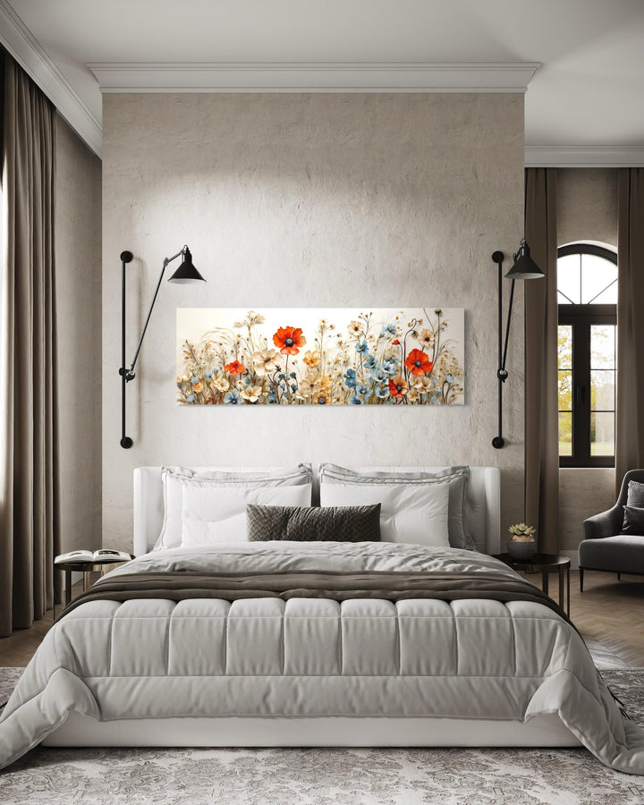 Long horizontal canvas wall art of poppies and blue flowers hanging above a bed in a modern room.