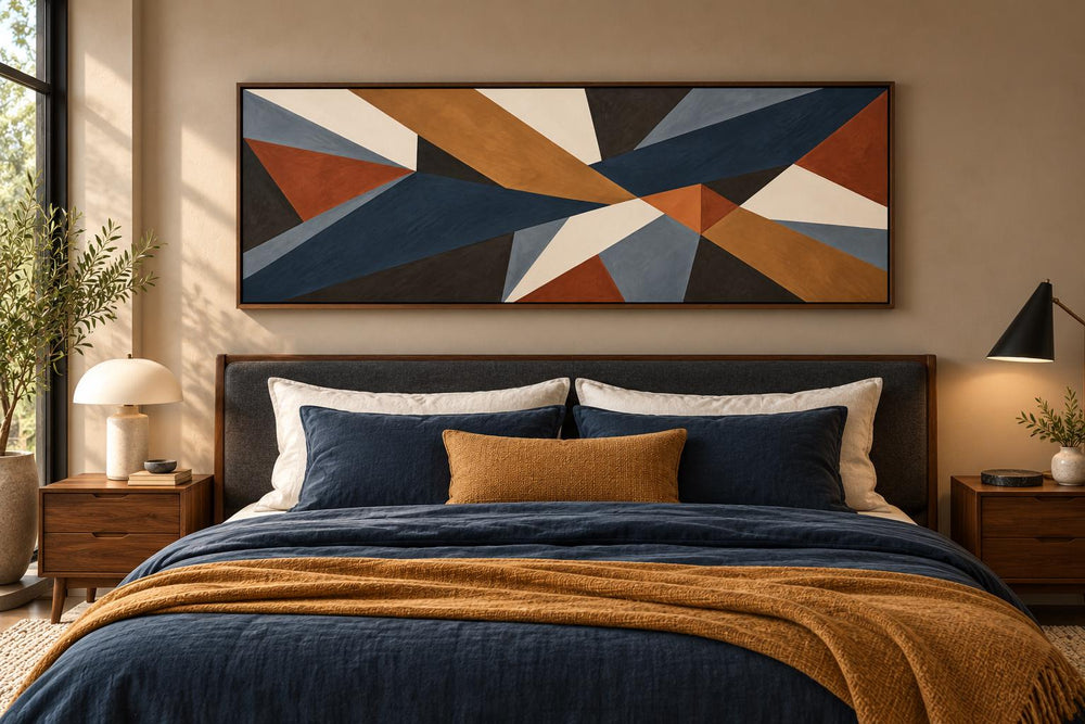 Long horizontal geometric abstract canvas wall art in earth tones above a bed with blue bedding.