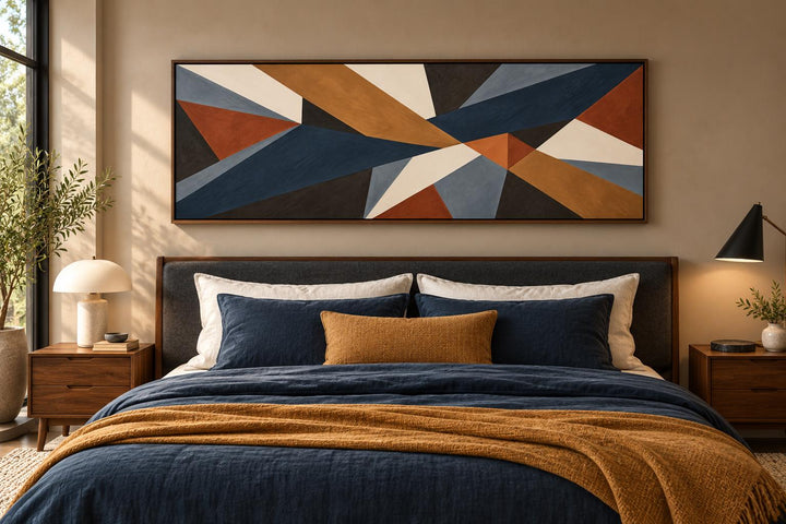 Long horizontal geometric abstract canvas wall art in earth tones above a bed with blue bedding.