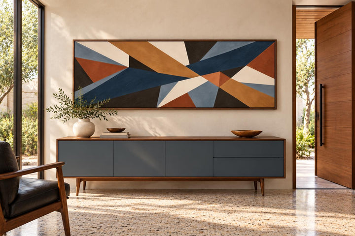 Long horizontal geometric abstract canvas wall art in earth tones above a blue mid-century sideboard.