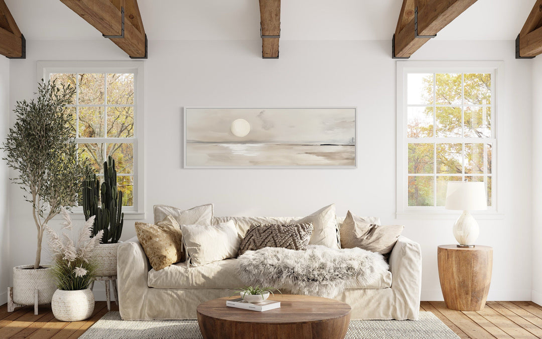 Long horizontal neutral coastal landscape wall art with a moon above a sofa in a rustic room.