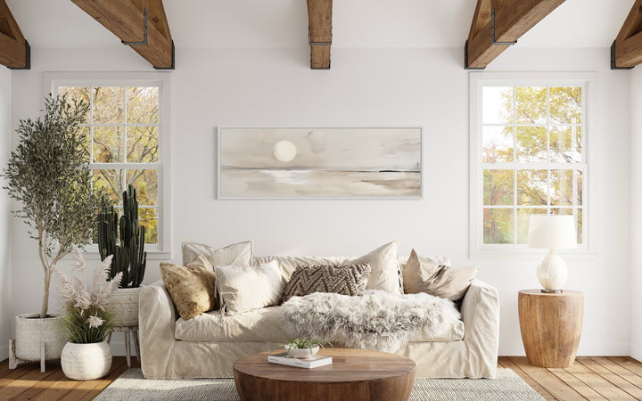 Long horizontal neutral coastal landscape wall art with a moon above a sofa in a rustic room.
