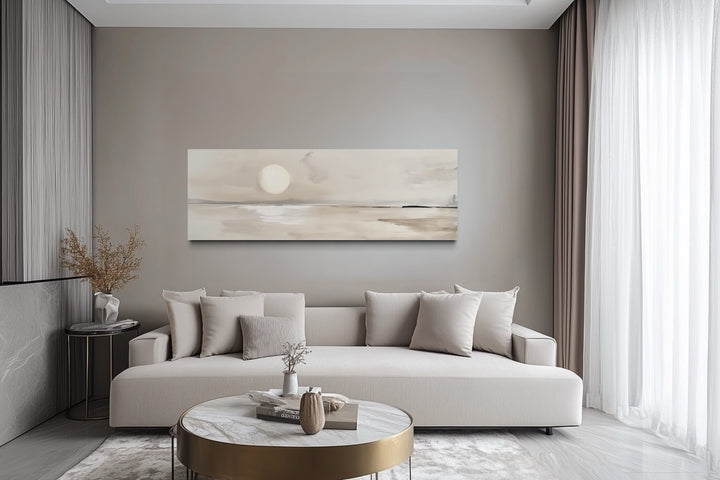 Long horizontal neutral coastal landscape canvas wall art with a moon above a sofa in a modern room.