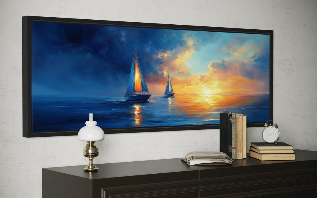 Long horizontal canvas wall art of sailboats on a blue ocean during a vibrant orange sunset.