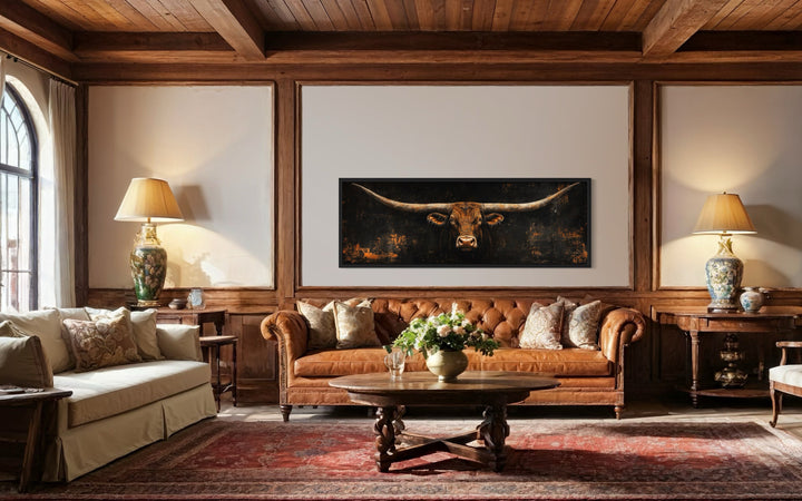 Long horizontal Texas longhorn bull head on black rustic canvas wall art above a leather sofa.