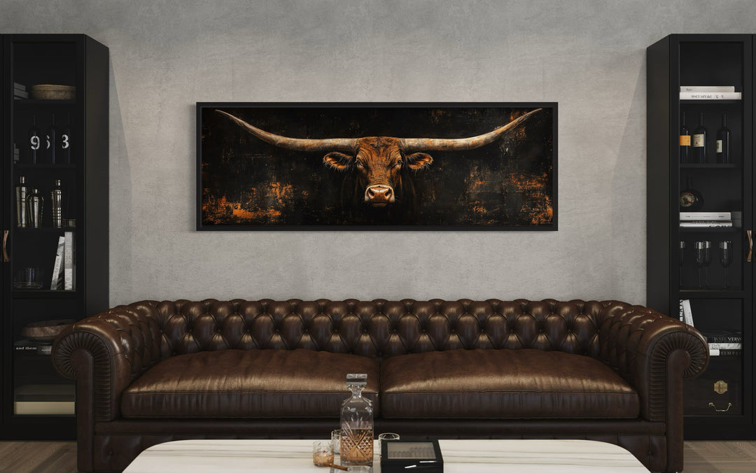 Long horizontal Texas longhorn bull head canvas wall art above a brown leather chesterfield sofa.