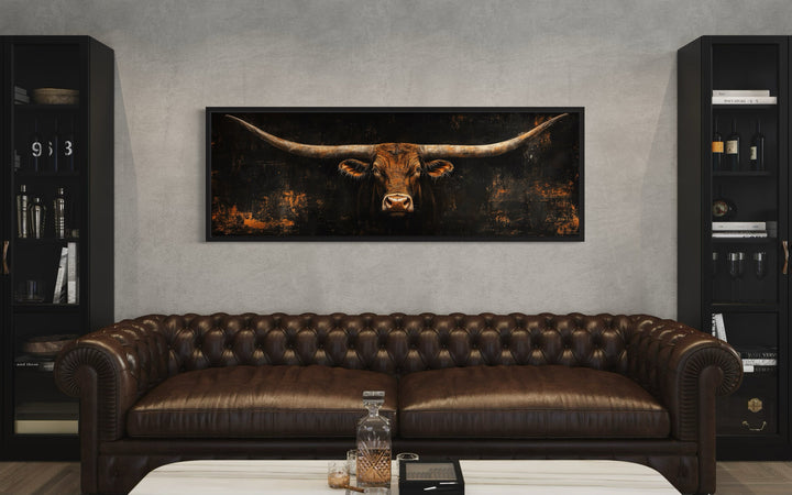 Long horizontal Texas longhorn bull head canvas wall art above a brown leather chesterfield sofa.