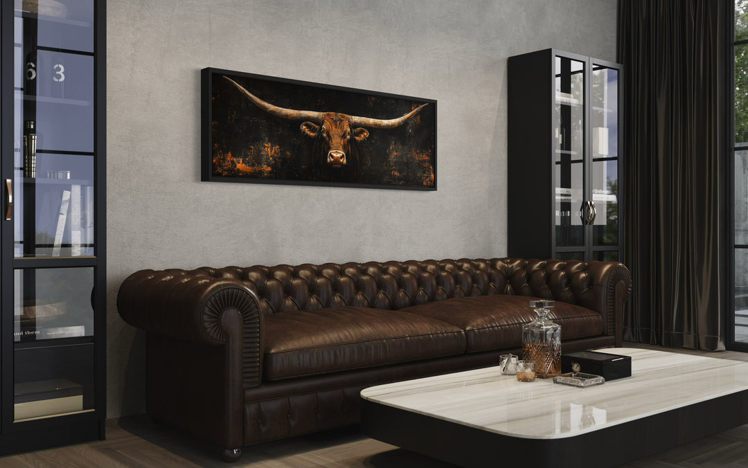 Long horizontal Texas longhorn bull head canvas wall art hanging above a brown leather sofa.