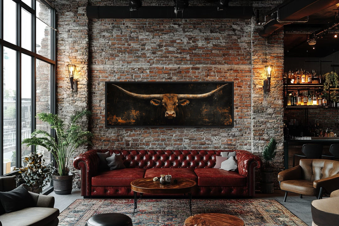 Long horizontal Texas longhorn bull head on black rustic canvas wall art above a red leather sofa.