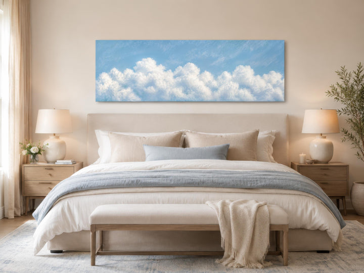 Long horizontal white cloud painting on blue sky canvas above a bed in a coastal bedroom.