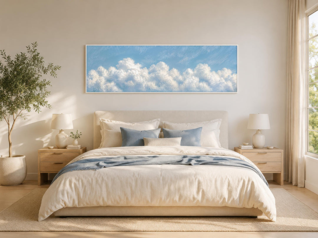 Long horizontal white cloud painting on blue sky canvas above a bed in a coastal bedroom.