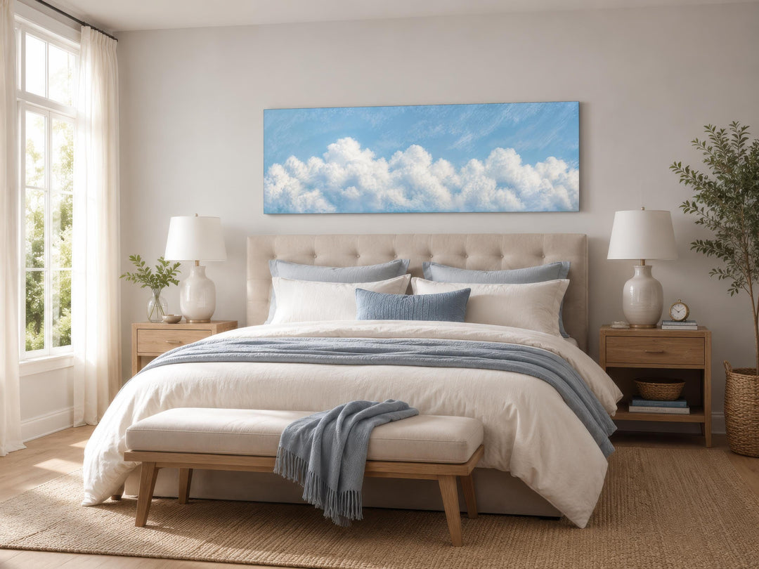 Long horizontal white cloud painting on blue sky canvas above a bed in a coastal bedroom.
