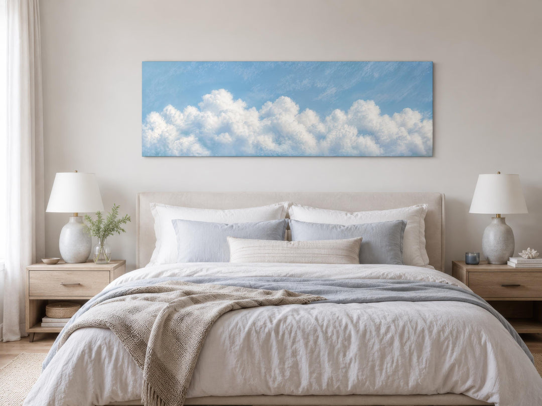 Long horizontal white cloud painting on blue sky canvas above a bed in a coastal bedroom.