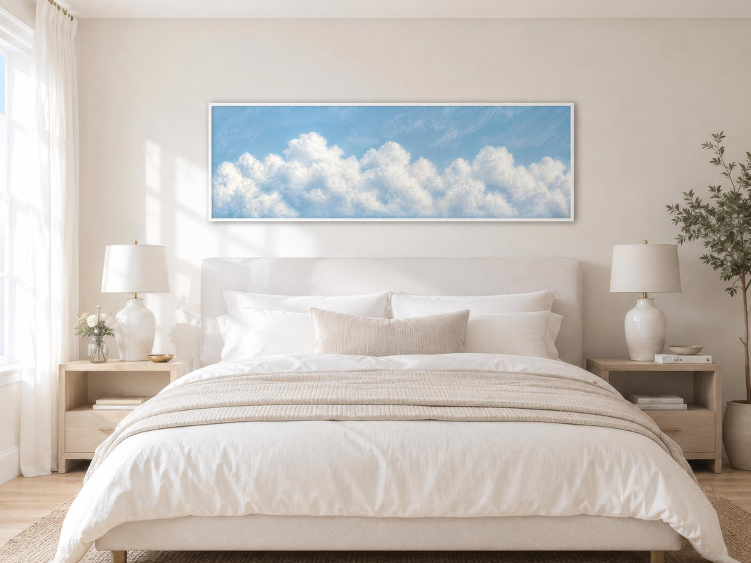 Long horizontal white cloud painting on blue sky canvas above a bed in a coastal bedroom.