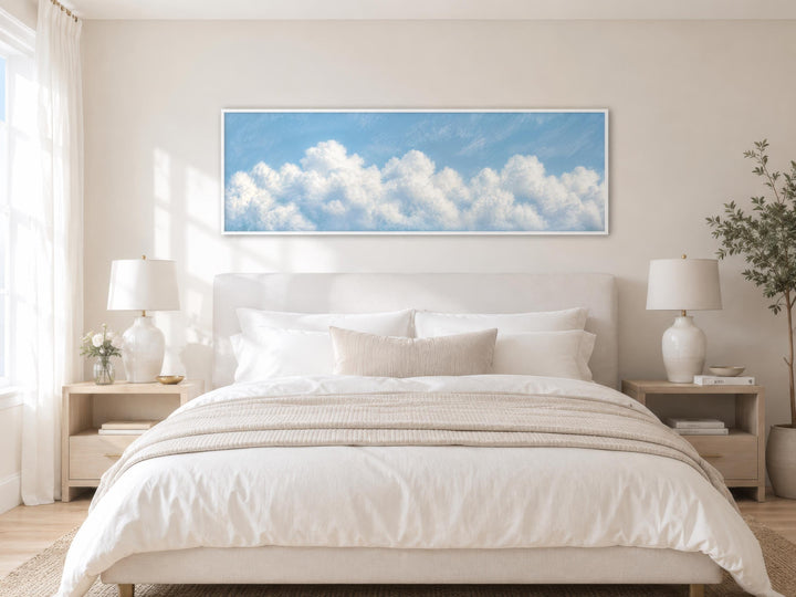 Long horizontal white cloud painting on blue sky canvas above a bed in a coastal bedroom.